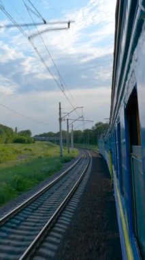 Kırsal kesimde hareket halindeki trenden, demiryolu eğrisi ve elektrik hatlarını gösteren yolcu treni penceresinden yan görünüm