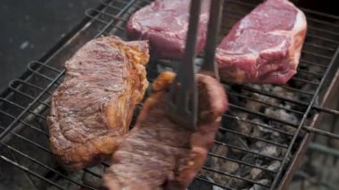 Kömürlü ızgaranın üstünde ızgara biftekler, açık hava barbeküsü sırasında dumanlı kömür ızgarasında biftek çevirme.