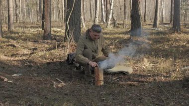 Ormanda Doğal Malzemeleri Kullanarak Ateş Yapan Bushcraft Adamı, ilkel kamp ateşi hazırlığı sırasında dumanla açık havada hayatta kalma pratiği