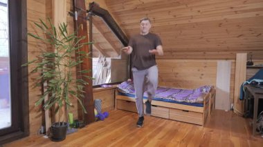 Ahşap tavan arasında kardiyo egzersizi yapan adam, kalp atışı, dayanıklılık ve günlük fitness rutinine odaklanmış aktif ev eğitimi.
