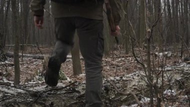 Bir insan kış ormanlarında yürüyor, düşen kütüklerin üzerinden geçiyor ve yapraksız ağaçlarda geziniyor. Zemin kısmen karla kaplı, sakin bir atmosfer yaratıyor..