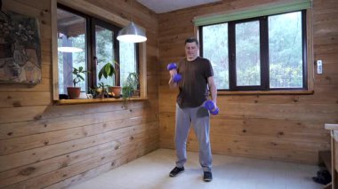 Ev içi güç egzersizi sırasında dambılları kaldıran bir adam günlük kuvvet antrenmanının bir parçası olarak evde biseptik kıvrımlar yapıyor.