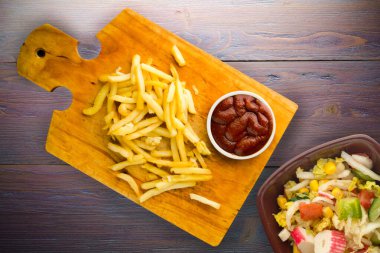 Patates kızartması ve mor ahşap arka planda ketçap. Kahverengi ahşap tabakta patates kızartması ve vejetaryen salata.