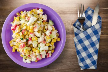 Mor tabakta çatal ve bıçak manzaralı yengeç salatası. Kahverengi ahşap arka planda yengeç salatası