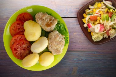 Limonlu patatesli pirzola ve sebze salatası. Patatesli pirzola ve mor ahşap arka plan.