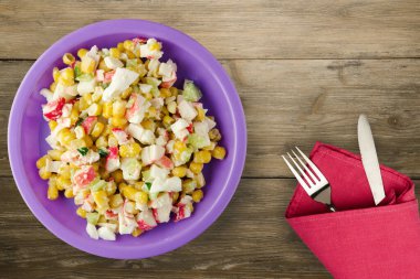 Mor tabakta çatal ve bıçak manzaralı yengeç salatası. Kahverengi ahşap arka planda yengeç salatası