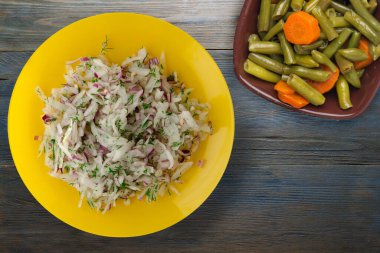 salata daikon, soğan ve dereotu mavi gri ahşap arka planda. Vejetaryen salsd soslu sarı tabakta salata.