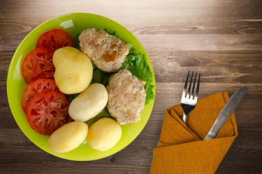 Kireç tabağında patates ve çatal ve bıçak manzaralı pirzola. Kahverengi ahşap arka planda patatesli pirzola