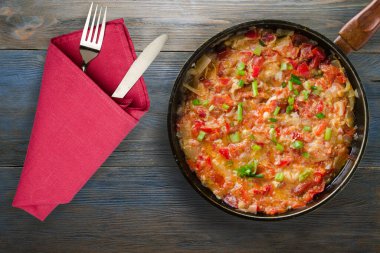 Gri mavi ahşap arka planda soğanlı haşlanmış domatesler. Metal tepsi manzaralı soğanlı haşlanmış domates. Çatal ve bıçakla vejetaryen yemeği