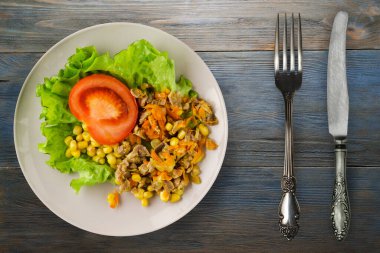Tavuk mideli salata, havuç, mısır ve çatal ve bıçak manzaralı açık gri tabakta salata. Mavi ahşap arka planda sebzeli tavuk salatası.