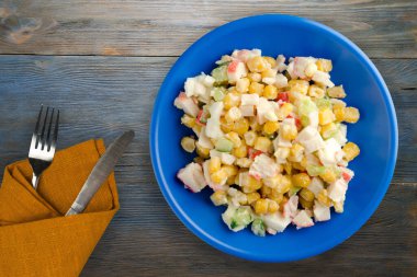 Çatal ve bıçak manzaralı lacivert tabakta yengeç salatası. Gri ve mavi ahşap arka planda yengeç salatası