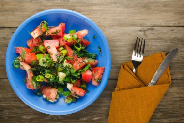 Çatal ve bıçak manzaralı mavi tabakta vejetaryen yemeği. Domates, soğan, kahverengi ahşap kaplama bir tabakta rezene. sağlıklı yiyecekler