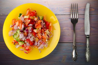 Vejetaryen yemeği. Biberli salata, domates, soğan, sarı tabakta brokoli. Mor ahşap arka planda vegan salatası. Çatal ve bıçaklı salata.