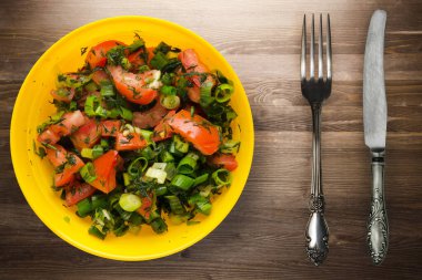 Bıçak ve çatalla vejetaryen yemeği. Domates, soğan, kahverengi ahşap arka planda sarı tabakta rezene. sağlıklı yiyecek üst görünümü