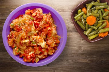 Kahverengi ahşap arka planda mor tabakta soğanlı haşlanmış domatesler. Soğan manzaralı haşlanmış domates. Sebze salatalı vejetaryen yemeği