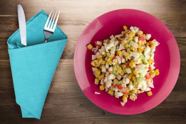 Çatal ve bıçak manzaralı kırmızı tabakta yengeç salatası. Kahverengi ahşap arka planda yengeç salatası