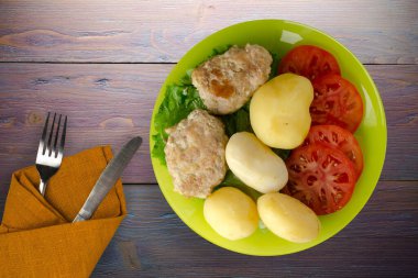 Kireç tabağında patates ve çatal ve bıçak manzaralı pirzola. Patatesli pirzola ve mor ahşap arka plan.