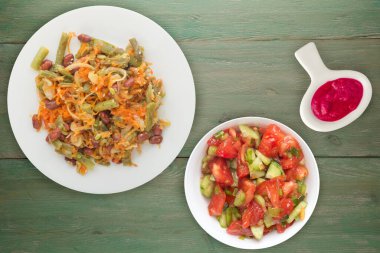 Vejetaryen salata manzarası. Sağlıklı yiyecekler. Fasulye salatası, kuşkonmaz, soğan, havuç ve susam yeşil ahşap arka planda beyaz bir tabakta..
