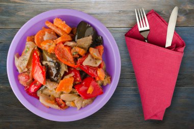 Mavi gri ahşap arka planda sebze güveci. Mor tabakta çatal ve bıçak manzaralı Bulgarca güveç