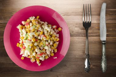 Çatal ve bıçak manzaralı kırmızı tabakta yengeç salatası. Kahverengi ahşap arka planda yengeç salatası