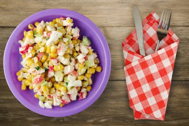 Mor tabakta çatal ve bıçak manzaralı yengeç salatası. Kahverengi ahşap arka planda yengeç salatası