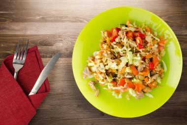  Tavuk mideli salata ile sebze havuç, soğan, biber, lahana, domates, brokoli. Kireç tabağında tavuk salatası, kahverengi ahşap arka planda çatal ve bıçak manzaralı.