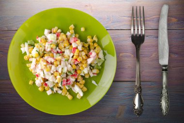 Kireç tabağında yengeç salatası, çatal ve bıçak manzaralı. Mor ahşap arka planda yengeç salatası