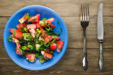 Çatal ve bıçak manzaralı mavi tabakta vejetaryen yemeği. Domates, soğan, kahverengi ahşap kaplama bir tabakta rezene. sağlıklı yiyecekler