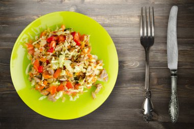 Tavuk mideli salata ile sebze havuç, soğan, biber, lahana, domates, brokoli. Limonlu tavuklu salata siyah ahşap arka planda çatal ve bıçak manzaralı.