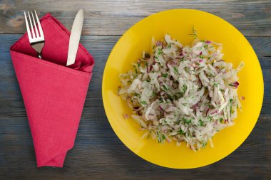 salata daikon, soğan ve dereotu mavi gri ahşap arka planda. Çatal ve bıçak manzaralı sarı tabakta salata.