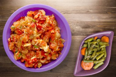 Kahverengi ahşap arka planda mor tabakta soğanlı haşlanmış domatesler. Soğan manzaralı haşlanmış domates. Sebze salatalı vejetaryen yemeği