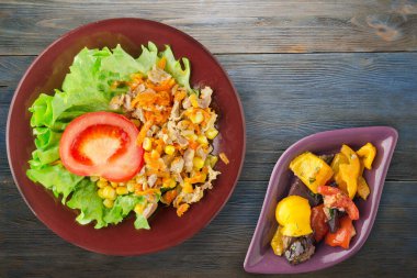 Tavuk mideli salata, havuç, mısır ve salata. Kahverengi tabak manzaralı. Mavi ahşap arka planda sebzeli tavuk salatası.
