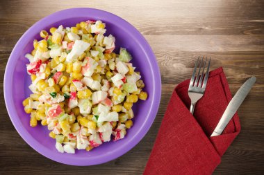 Mor tabakta çatal ve bıçak manzaralı yengeç salatası. Kahverengi ahşap arka planda yengeç salatası