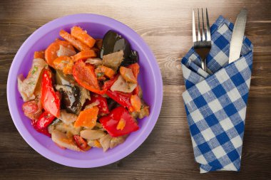 Kahverengi ahşap arka planda sebze güveci. Mor tabakta çatal ve bıçak manzaralı Bulgarca güveç