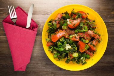 Bıçak ve çatalla vejetaryen yemeği. Domates, soğan, kahverengi ahşap arka planda sarı tabakta rezene. sağlıklı yiyecek üst görünümü