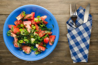 Çatal ve bıçak manzaralı mavi tabakta vejetaryen yemeği. Domates, soğan, kahverengi ahşap kaplama bir tabakta rezene. sağlıklı yiyecekler