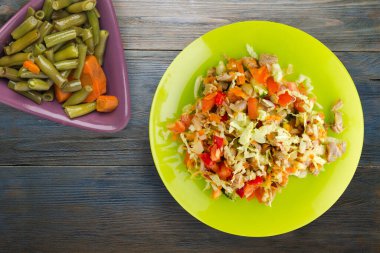 Tavuk mideli salata ile sebze havuç, soğan, biber, lahana, domates, brokoli. Sarı tabakta tavuklu salata. Mavi ahşap arka planda. Vejetaryen yemeği.