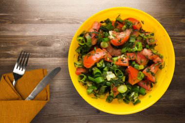 Bıçak ve çatalla vejetaryen yemeği. Domates, soğan, kahverengi ahşap arka planda sarı tabakta rezene. sağlıklı yiyecek üst görünümü