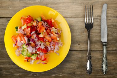 Vejetaryen yemeği. Biberli salata, domates, soğan, sarı tabakta brokoli, çatal ve bıçak üst görüşü. Tahta arka planda vejetaryen salatası