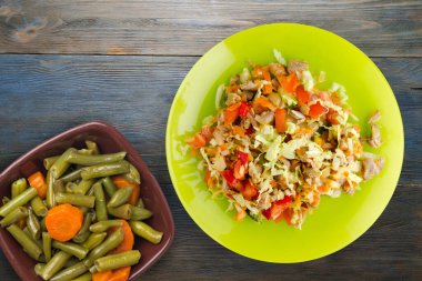 Tavuk mideli salata ile sebze havuç, soğan, biber, lahana, domates, brokoli. Sarı tabakta tavuklu salata. Mavi ahşap arka planda. Vejetaryen yemeği.
