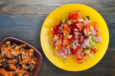 Vejetaryen yemeği. Biberli salata, domates, soğan, sarı tabakta brokoli. Mavi gri ahşap arka planda vegan salatası