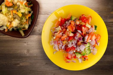 Vejetaryen yemeği. Biberli salata, domates, soğan, sarı tabakta sebze salatası manzaralı brokoli. Kahverengi ahşap arka planda vegan salatası