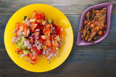 Vejetaryen yemeği. Biberli salata, domates, soğan, sarı tabakta brokoli. Mavi gri ahşap arka planda vegan salatası