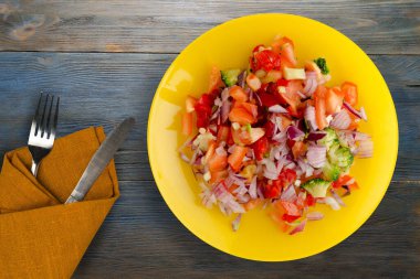 Vejetaryen yemeği. Biberli salata, domates, soğan, sarı tabakta brokoli. Mavi gri ahşap arka planda vegan salatası