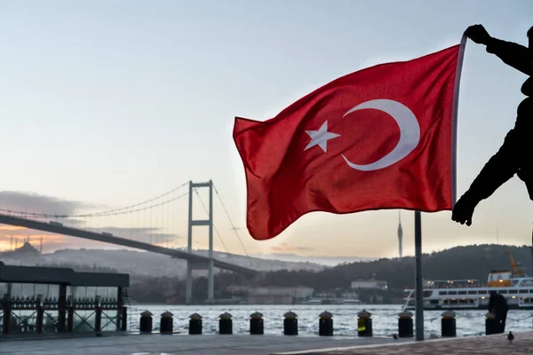 Man silhouette hold Turkish Flag in front of 15th July Martyrs Bridge (in Turkish 15 Temmuz Sehitler Koprusu ) or Bosphorus Bridge in Istanbul, Turkey. Patriotism concept.