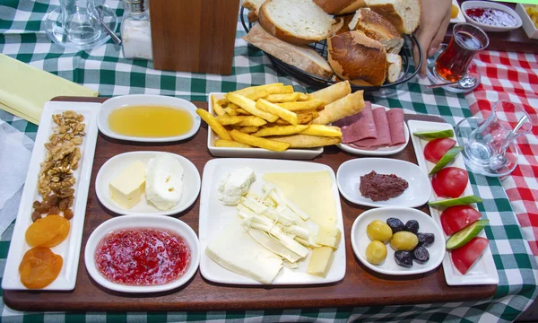 Family having delicious rich traditional Turkish breakfast include tomatoes, cucumbers, cheese, butter, eggs, honey, bread, olives, jam, sausage, fried potatoes and tea cups.