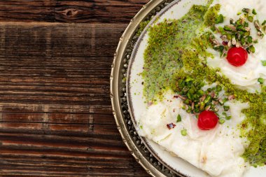 Traditional Turkish milky Ramadan Dessert named Gullac with sugar, powder of pistachio, milk and gullac sheets (rice wafer or rice paper sheets) on vintage metal plate and wooden background. clipart