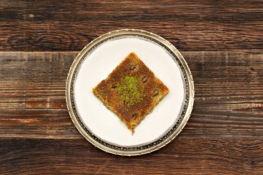 Geleneksel Türk tatlısına yakın plan: Ahşap zemin üzerinde fıstık tozu (Burma kadayif) bulunan Kadayif. Ramazan ayının en popüler tatlısı (Türkçe: Ramazan bayrami).