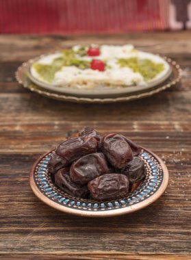 Fresh date fruits in ottoman handmade bowl on the front and Traditional Turkish milky Ramadan Dessert named Gullac on the background. White wooden background. Ramadan (Ramazan) food for iftar or sahur clipart