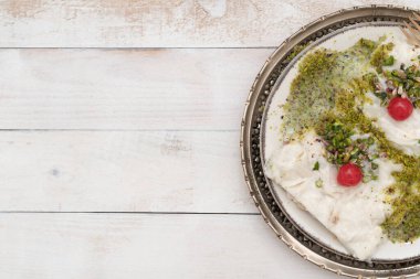 Geleneksel Türk sütlü Ramazan Tatlısı, klasik metal tabak ve beyaz ahşap zemin üzerinde şeker, şam fıstığı tozu, süt ve gullac çarşafı (pirinç gofreti veya pirinç kağıdı) ile adlandırıldı.